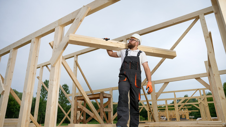 A worker carrying a wooden beam on a construction site for a timber home