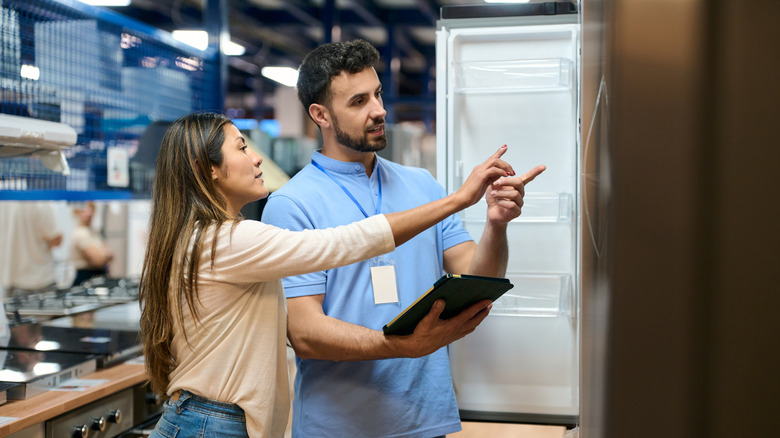 a store technician shows a customer the details on a side-by-side refrigerator