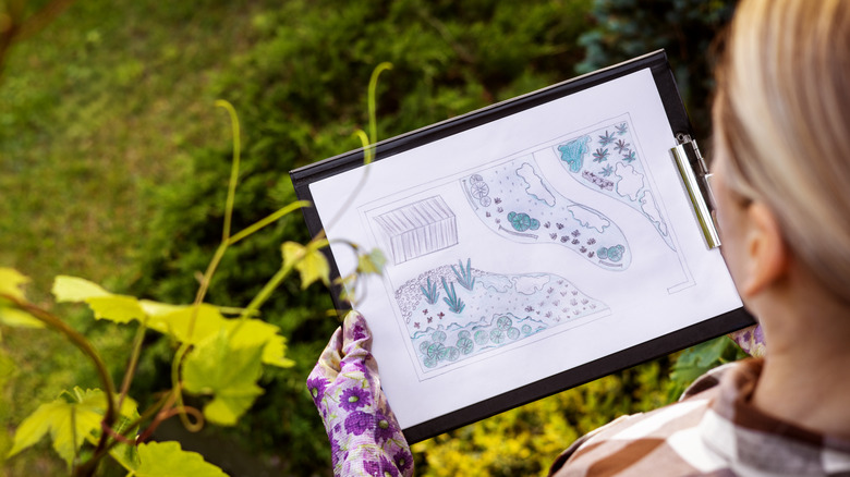 A designer holds a plan for a backyard renovation in her hands while standing outside.