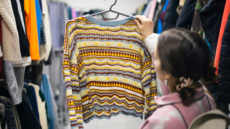 A person at a thrift store looking at an old sweater