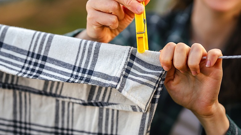 Close-up of a person clipping a piece of clothing to a clothesline with a yellow clothespin