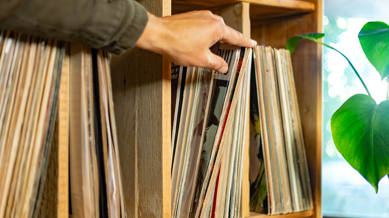 A hand flips through vinyl records on a shelf