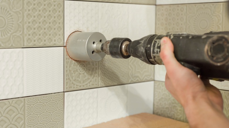 person drilling hole into tiled wall