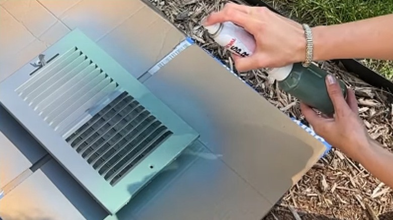A person using the small paint sprayer to spray paint a wall vent