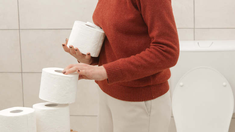 Woman stacking toilet paper in a bathroom.