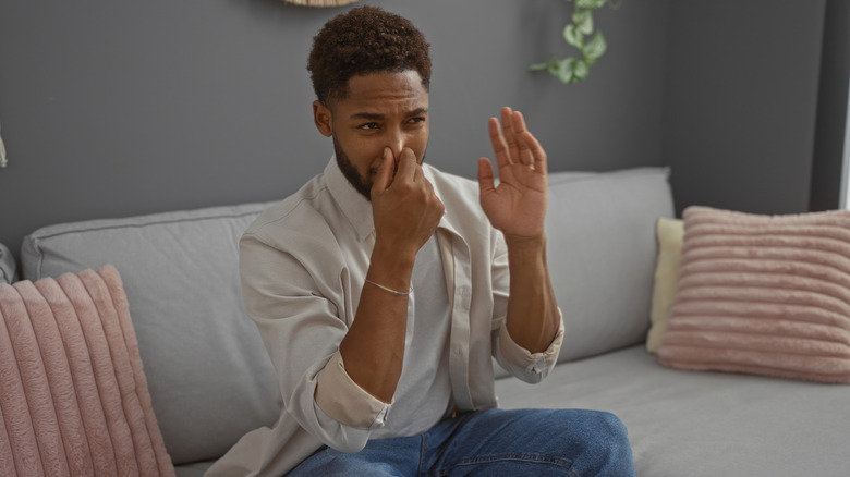 Man holding his nose sitting on couch with bad odor