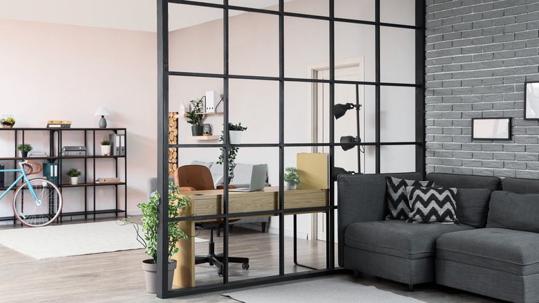 Stylish, modern home with a dark, metal open window frame as room divider between the home office and living room