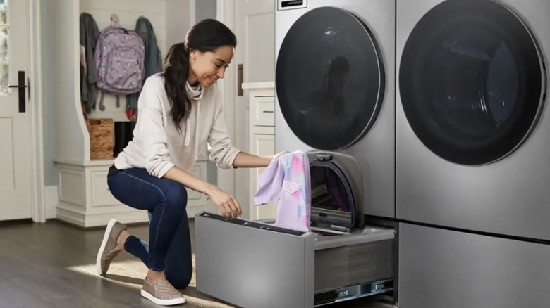 A woman uses the LG SideKick top load pedestal washer placed below a washing machine