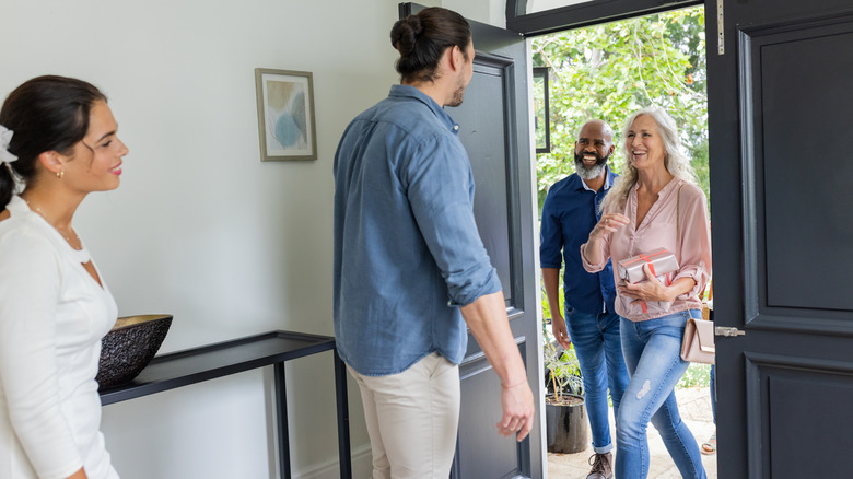 Man and woman welcoming two guests into home entryway