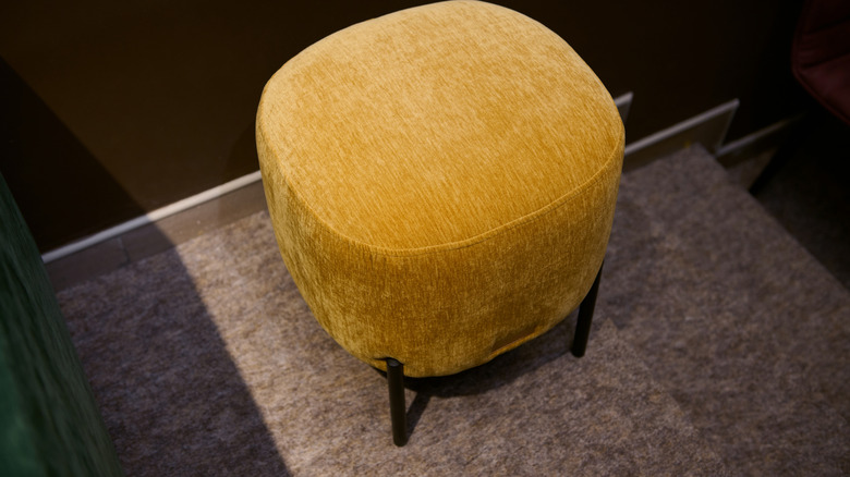 A yellow footstool sitting on top of a carpet.