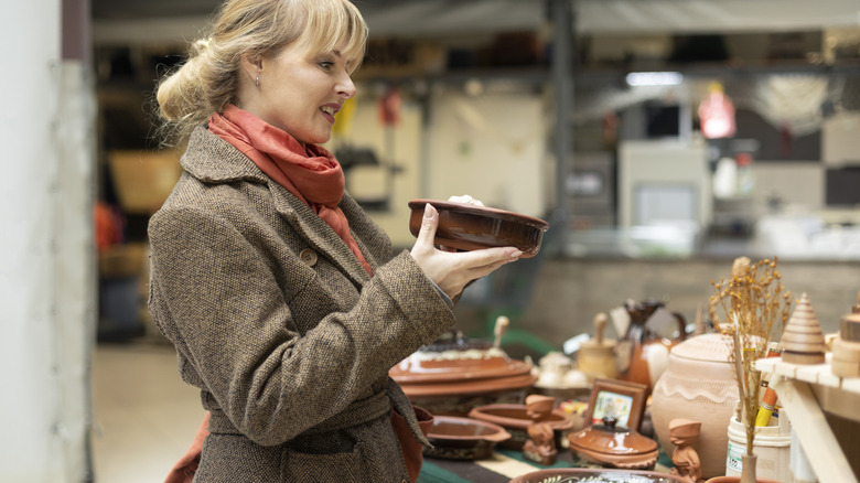 Woman in tweed coat and red scarf holding a bowl at a flea market.
