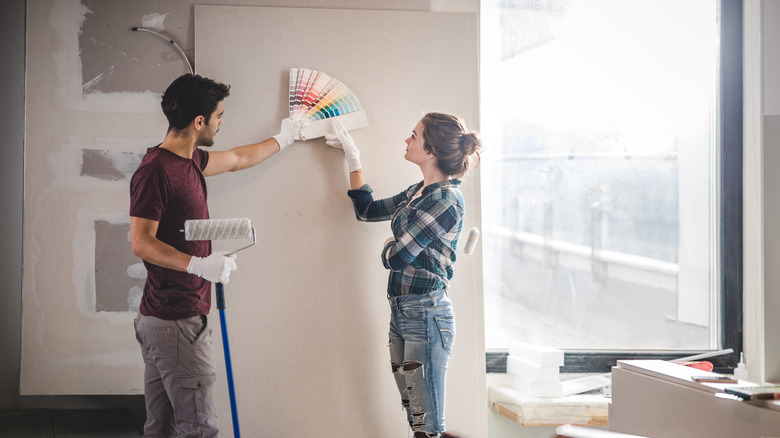 A couple holds colorful interior paint swatches up to the wall.