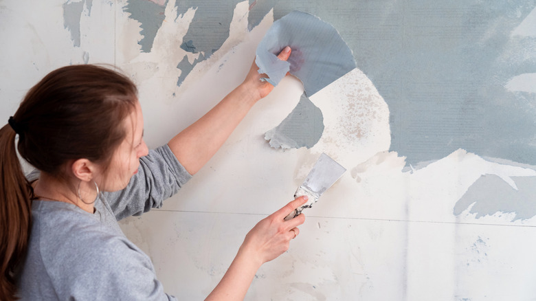 brunette woman removes blue wallpaper 