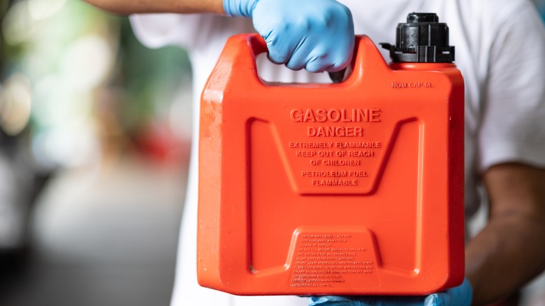 A man wearing latex gloves holds a red gas can in front of his body.