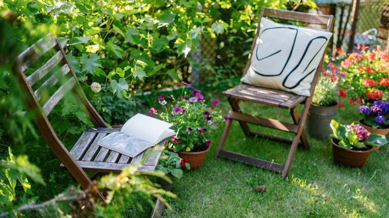 Two wooden chairs on a shaded green lawn with potted and wild plants.