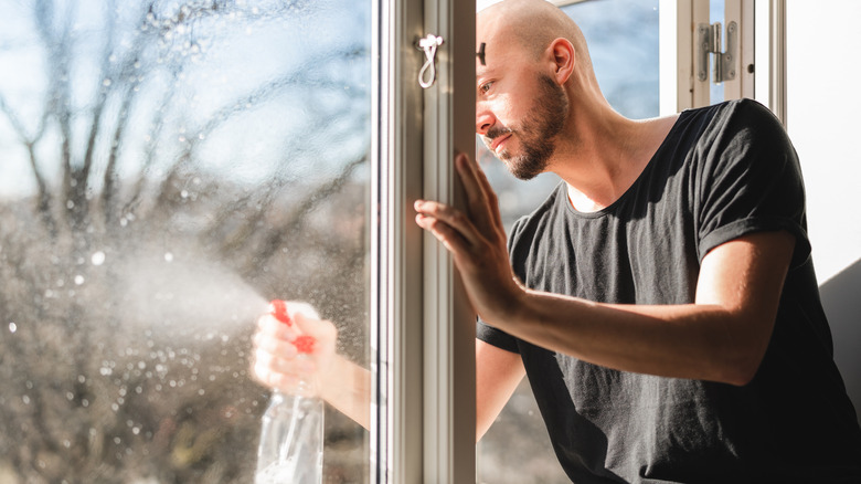 Man in black shirt spraying outside of window from inside home