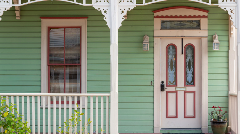 The porch of a green-paneled house with a white and red door