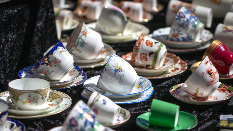 Antique teacups and saucers rest on black crushed velvet fabric