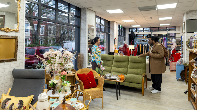 A female thrift shop employee assists a man looking at a green sofa