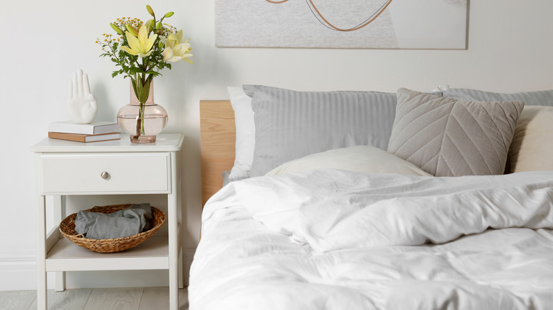 A neutral bedroom with a white nightstand holding a basket and decorative items.