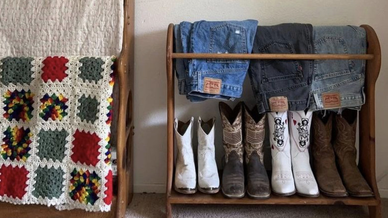 Wooden quilt rack repurposed to display three pairs of jeans and four pairs of cowboy boots next to another quilt rack with afghan