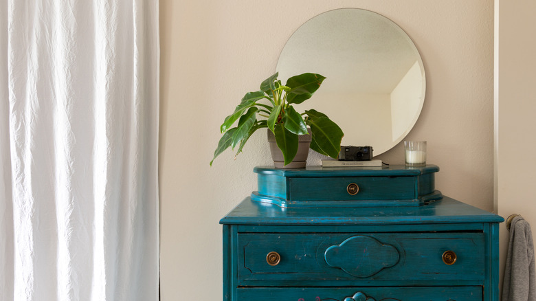 A vintage dresser painted teal with updated knobs and modern mirror.