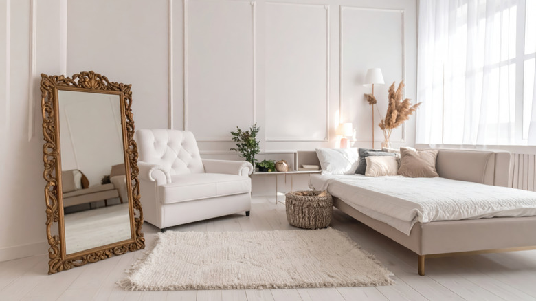 A white bedroom with a large ornate mirror propped up on the floor to the left