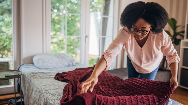 A woman folds a knitted blanket on her bed
