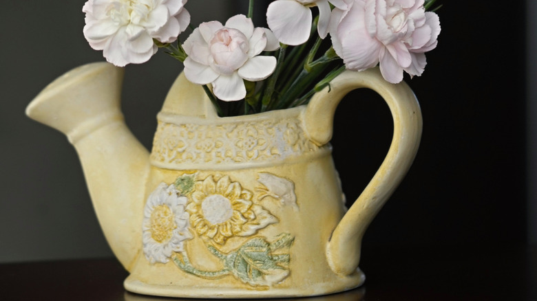 A small, yellow ceramic watering can filled with pink and white flowers