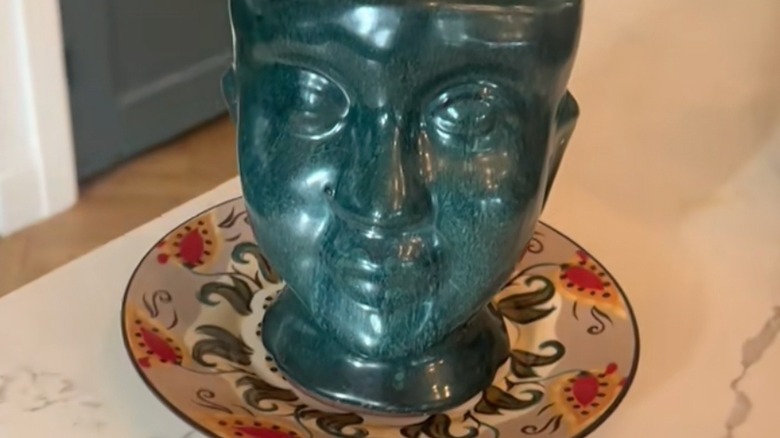 Closeup of a planter resembling a face with a decorative plate underneath