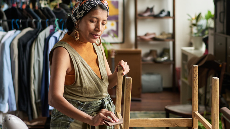 woman wiping down wooden side table in thrift store