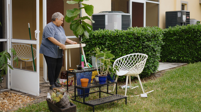 A woman moves furniture, plants, and other outdoor accessories from inside to a backyard patio.