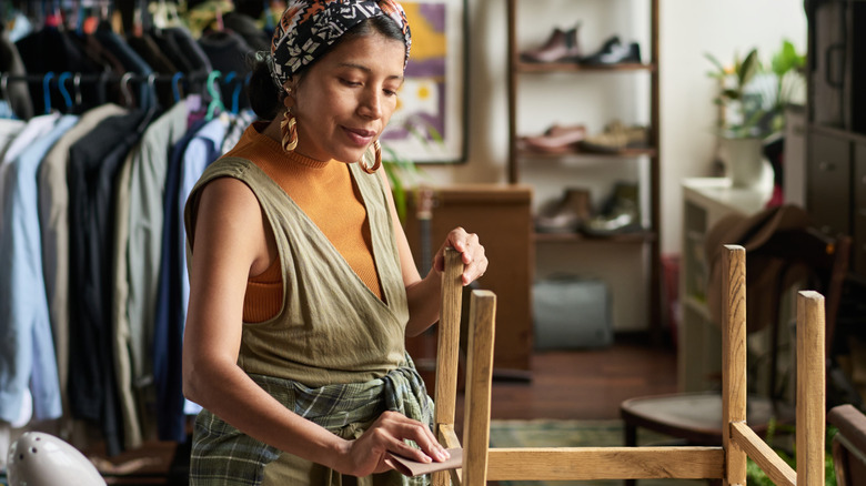 woman wiping down wooden side table in thrift store
