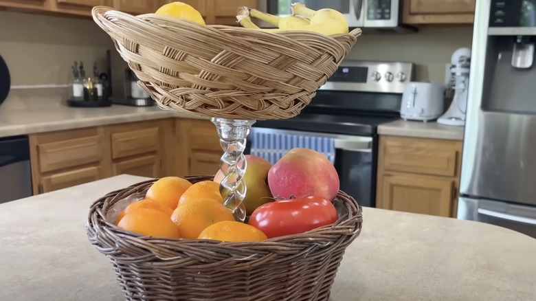 Tiered storage display holding fruit made from two wicker baskets and a candle holder