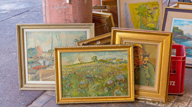A collection of vintage framed paintings sitting by a doorway