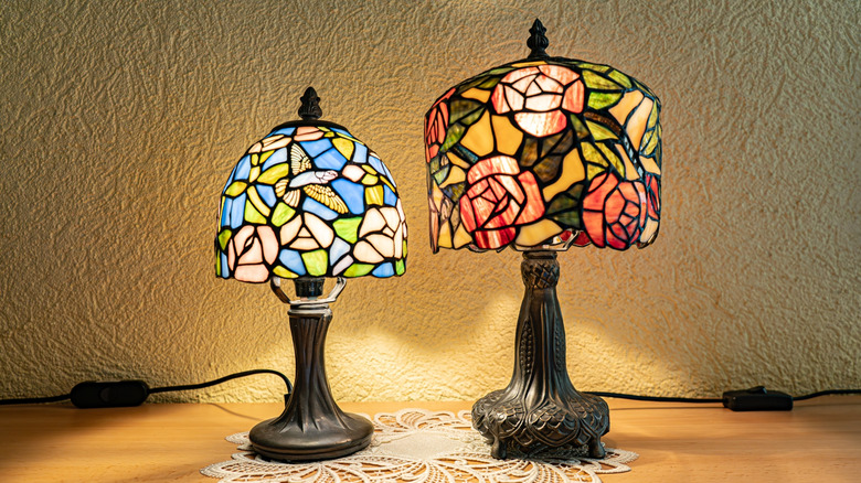 Two switched-on Tiffany-style lamps sit on lace doily on a wooden dresser.