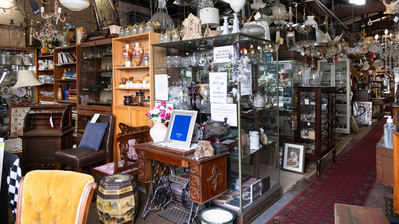 The cluttered inside of a thrift store full of vintage furniture and glassware