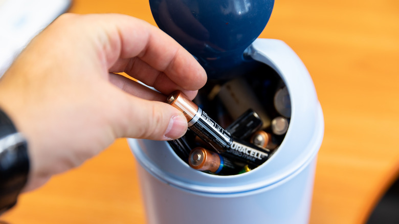 hand putting battery in garbage