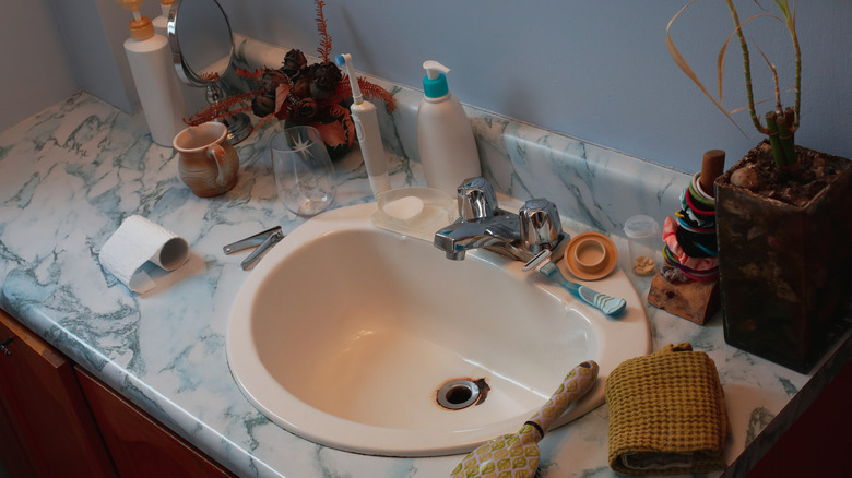 An outdated bathroom countertop cluttered with beauty and bath products.
