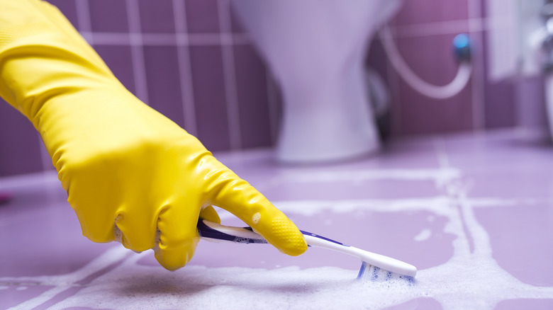 Gloved hand cleaning dirty grout