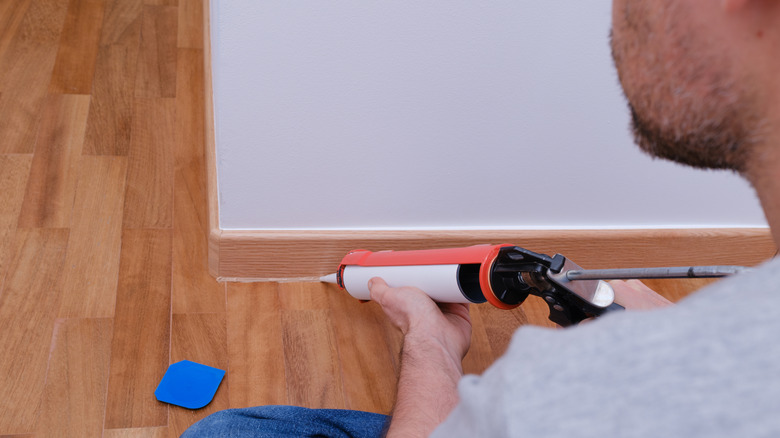 Man caulking gaps along wooden baseboard