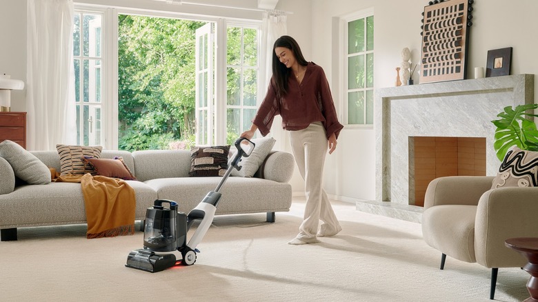 A woman using a carpet cleaner on a white carpet in the living room