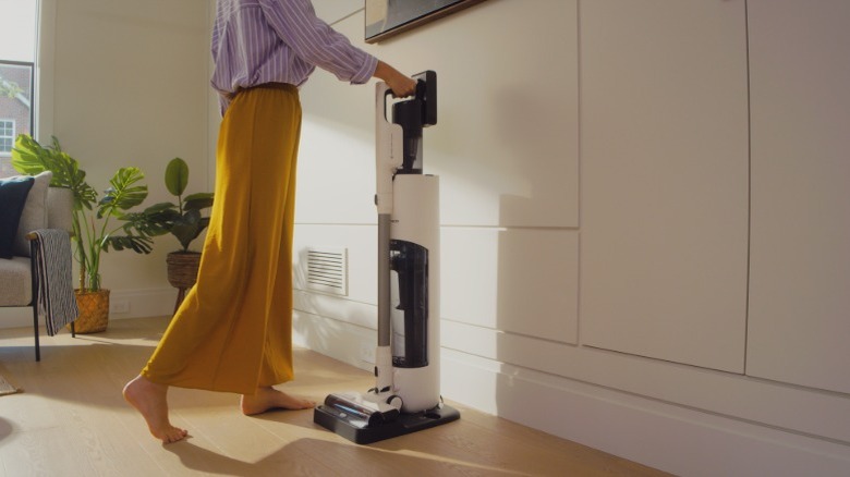 A person wearing yellow pants placing a vacuum cleaner in a dock