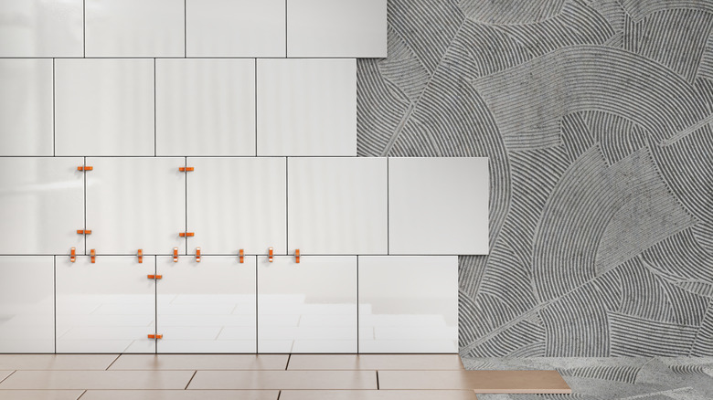 Plain white ceramic tile is being applied as the back wall over a countertop with long, brown tiles.