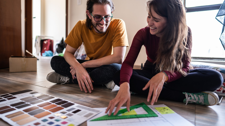 A smiling couple sitting on the floor and designing a room