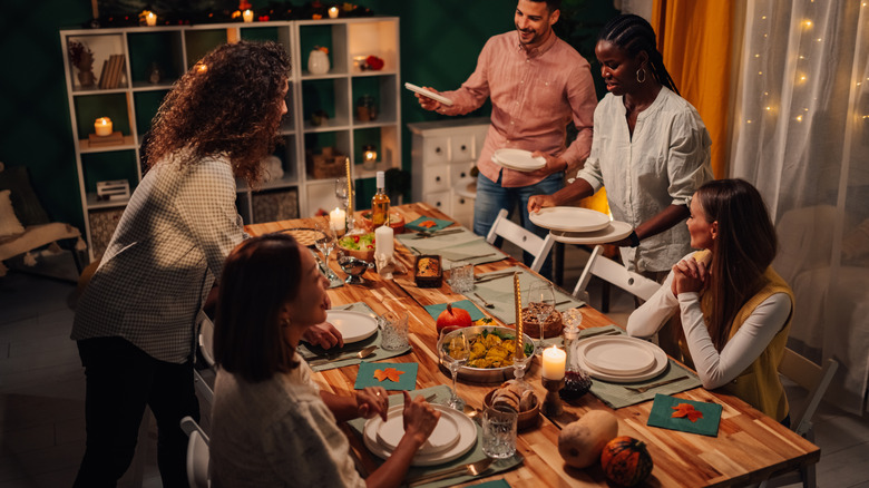 A group of people sitting and moving around a set dining table