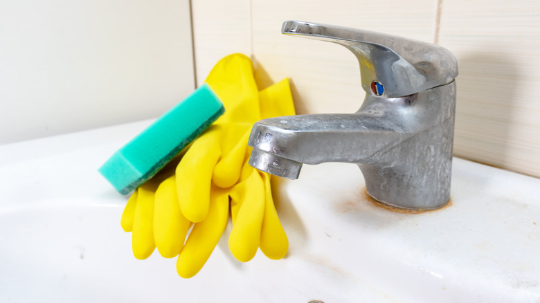 Rusted bathroom faucet with gloves and sponge