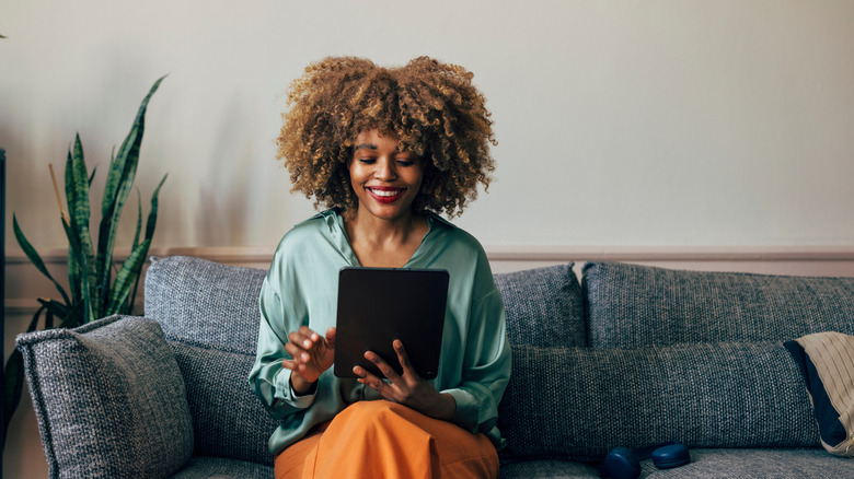 A woman sits on a blue sofa browsing on her tablet
