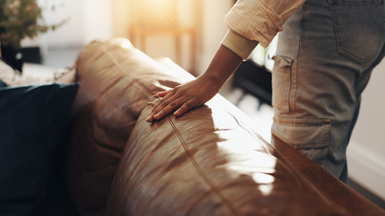 A person runs their hand over the back of a leather sofa cushion