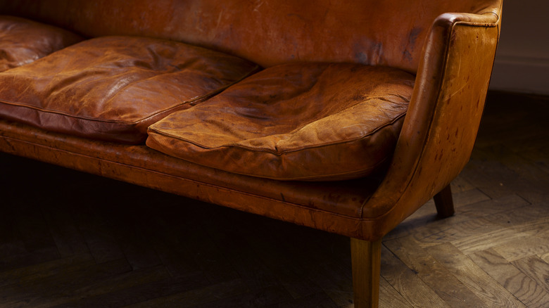 A brown leather sofa with smushed cushions and oil stains